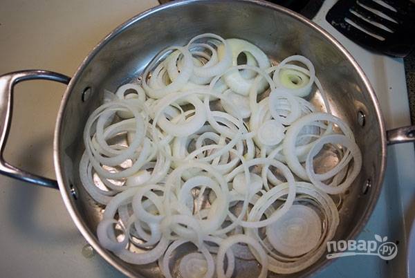 В кастрюле или чугунке, которые можно ставить в духовку, уложите лук, нарезанный кольцами. Должно быть минимум 2 слоя лука.