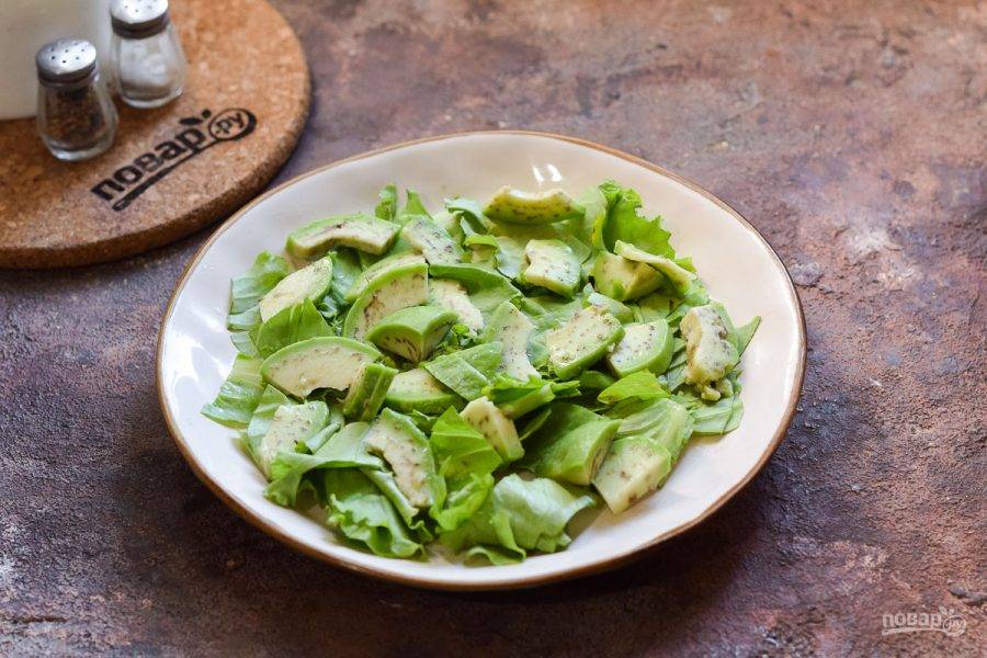 На тарелку выложите порванные руками салатные листья и авокадо.