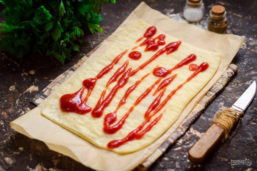 Слоеное тесто раскатайте и пропеките в духовке 4 минуты при температуре 180 градусов. Смажьте основу кетчупом.