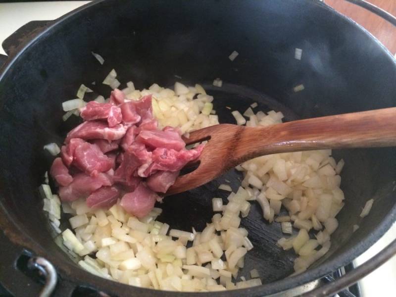 2.	В казанок выложите лук, обжаривайте его до появления легкого золотистого цвета. Нарежьте тем временем мякоть свинины и добавьте ее к луку. Обжаривайте мясо до готовности.