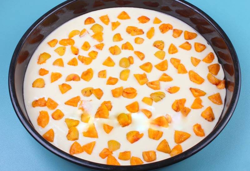 В смазанную маслом форму вылейте тесто, при необходимости слегка разровняйте, а затем выложите сверху абрикосы. Я режу их на кусочки в зависимости от размера, если они некрупные, можно просто разделить их на половинки.
