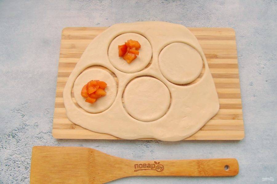 Тесто раскатайте в пласт и с помощью стакана или другой выемки вырежьте кружки. На середину кружков выложите кусочки абрикосов.
