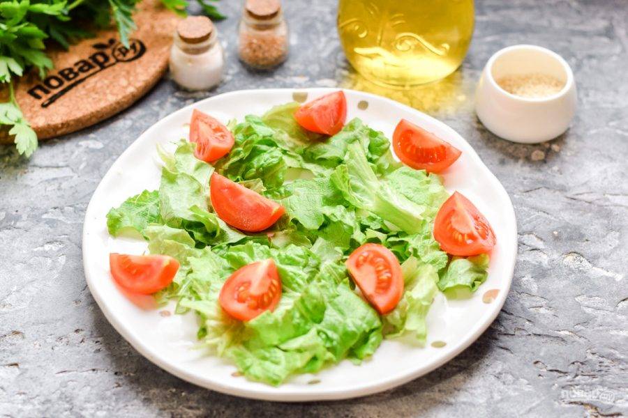 На тарелку выложите чистые, порванные руками салатные листья. Черри ополосните и нарежьте дольками, выложите в салат.