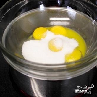 2. На плиту поставьте сотейник или кастрюлю с водой (воды налейте до половины посуды), доведите до кипения. Затем понизьте огонь до медленного. В миску, которая не провалится в кастрюлю с кипящей водой, всыпьте 1/4 стакана сахара и добавьте яичные желтки. Поставьте миску на кастрюлю. Убедитесь, что ее дно не находится в воде!