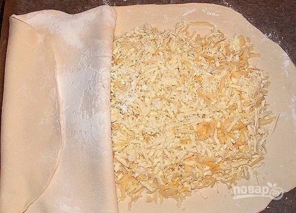 Выложите сырную начинку на расстеленный кусок теста на рабочей поверхности. Вниз лучше постелить пергамент для запекания или кулинарную бумагу. Накройте вторым куском и хорошенько защипните края. 