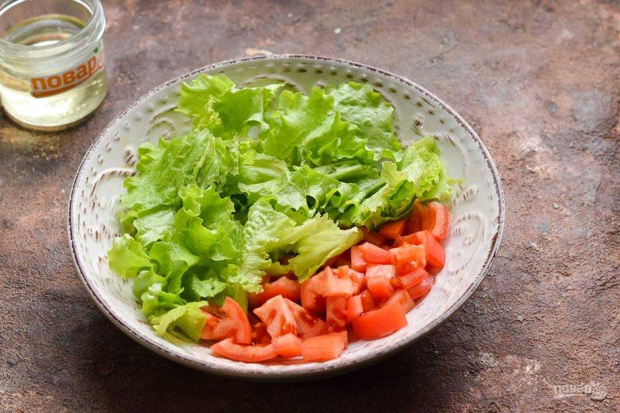 Переложите помидоры в тарелку, добавьте салатные листья, порванные руками.