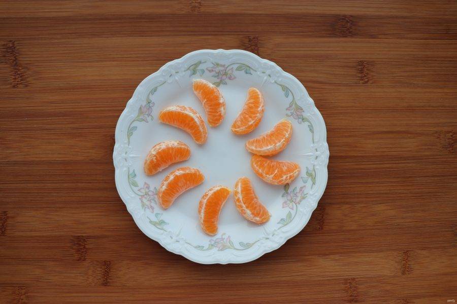Мандарин нам понадобится для украшения кексов. Очистите мандарин от кожуры и разложите дольки на тарелке, чтобы они немного подсохли, так их будет легче очистить от пленки. 
