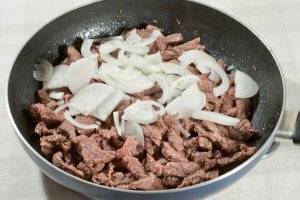 Добавьте к мясу, перемешайте и жарьте ещё 3-5 минут, до прозрачности лука.