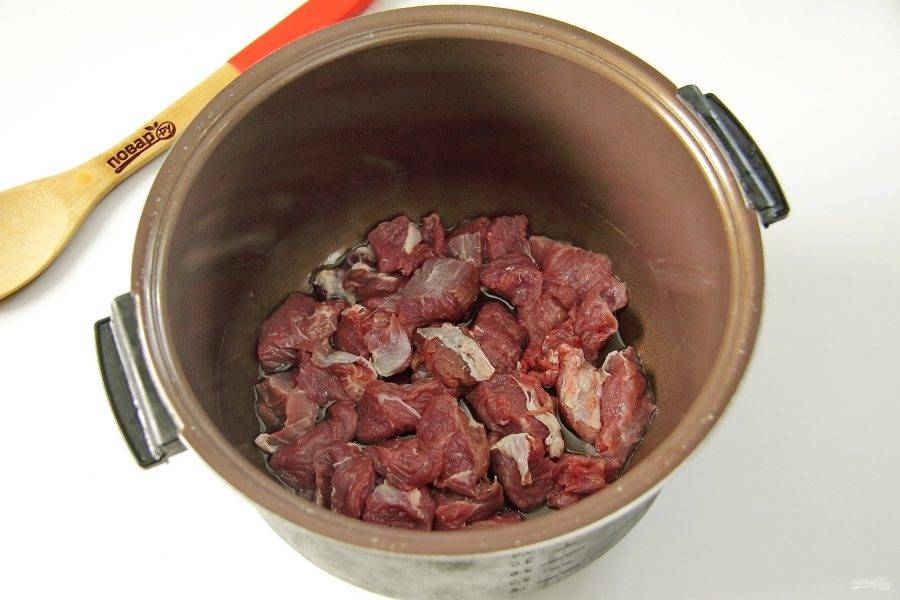 2. Мясо нарежьте небольшими кусочками, сложите в чашу мультиварки и добавьте масло.
