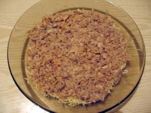 Первым делом нужно отварить картофель, морковь и яйца. Отваренные продукты остудить и почистить. На мелкой тёрке натереть картошку, морковку, белки, желтки и сыр (всё в отдельных мисочках или тарелках).
В салатницу выложить рыбу с маслом и размять вилкой по всей поверхности дна посуды. Сверху смазать небольшим количеством майонеза.