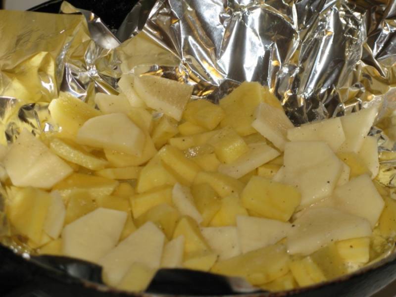Застелите сковороду фольгой. Картофель нарезаем тонкими пластинками и выкладываем несколькими слоями на фольгу. Солим и перчим по вкусу.