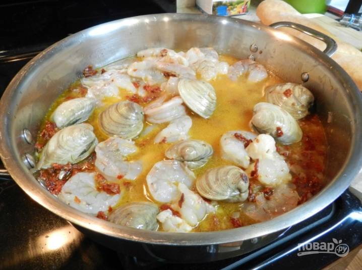 Через минуты 3 добавьте в сковороду морепродукты, влейте вино и позвольте жидкости выпариться. Ракушки должны открыться.