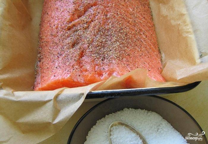 Кладем рыбу в удобную подходящую тару (у меня - форма для запекания), застланную пекарской бумагой. Щедро натираем рыбку солью, перцем и сахаром.