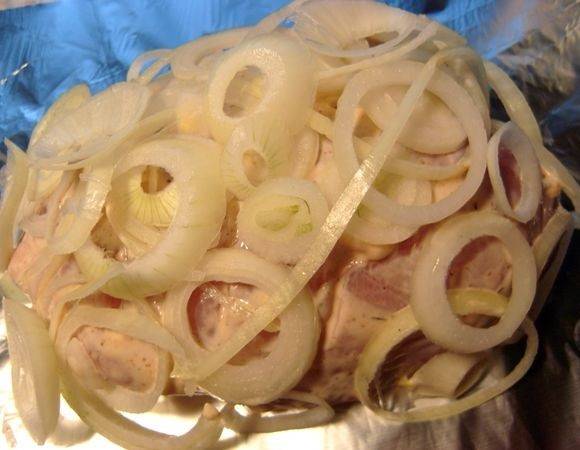 4. Очистить луковицу и нарезать тонкими кольцами. Обложить курочку со всех сторон луком, предварительно поместив ее на лист фольги.