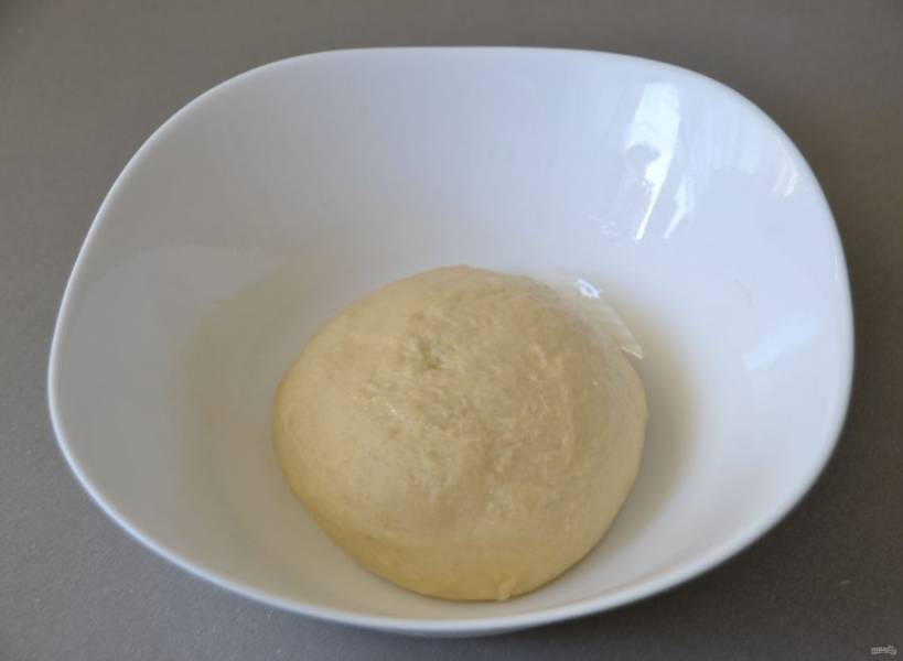 Смажьте миску растительным маслом, выложите в него тесто, накройте пищевой пленкой. Поставьте на расстойку примерно на 1,5 часа до удвоения объема. В процессе расстойки сделайте одну обминку теста. 