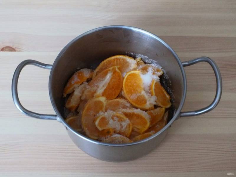 По истечении времени мандарины нарежьте на дольки, переложите в кастрюлю и засыпьте половиной указанного количества сахара. Перемешайте.