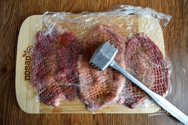 Накройте мясо пищевой пленкой и отбейте кухонным молоточком с двух сторон.