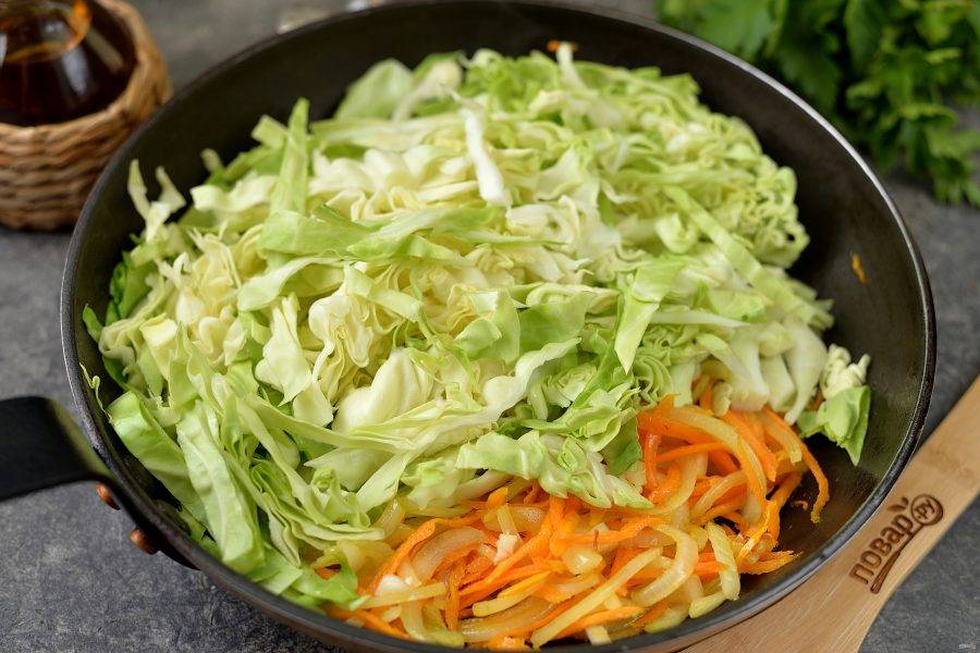 Выложите в сковороду нашинкованную капусту, перемешайте, обжарьте пару минут вместе с овощами.