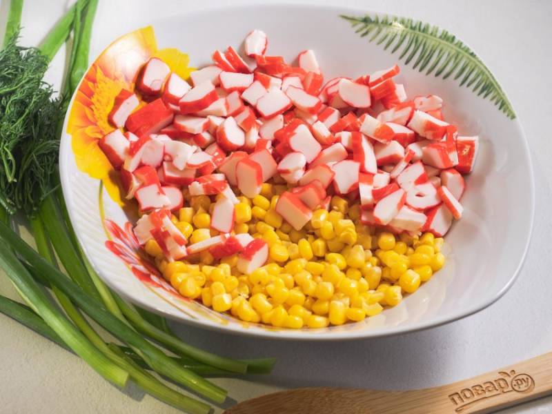 С кукурузы слейте жидкость и положите в салатник, крабовые палочки нарежьте и тоже добавьте в салатник.