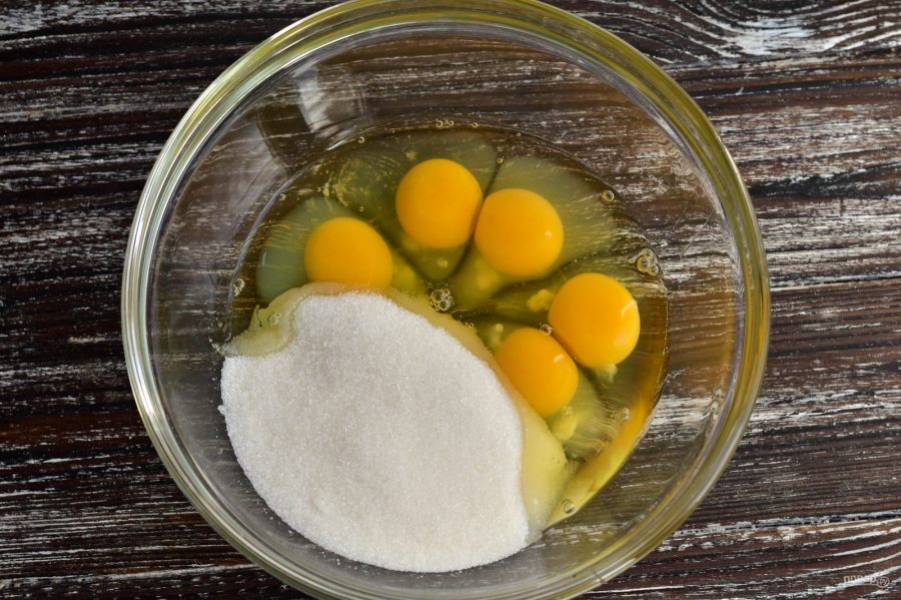 Вбейте куриные яйца в миску и сразу же всыпьте к ним сахар.