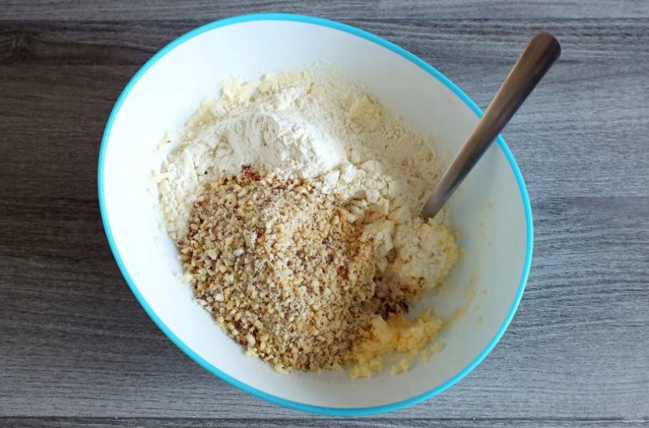 К масляно-яичной массе добавьте измельченные орехи и муку. Начните тесто замешивать с помощью вилки. Как только оно начнет собираться в комочки, месите руками.