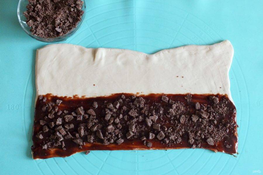 Визуально поделите пласт пополам. Половину теста смажьте обильно шоколадной массой. Посыпьте небольшой частью рубленого шоколада.