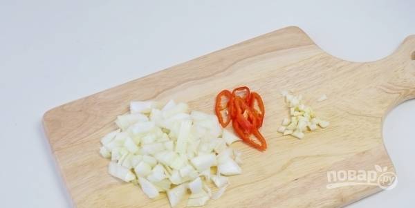 Очистите чеснок и лук. Нарежьте овощи на мелкие кубики. Затем вымойте красный острый перец. Нарежьте его кружочками вместе с семенами. 