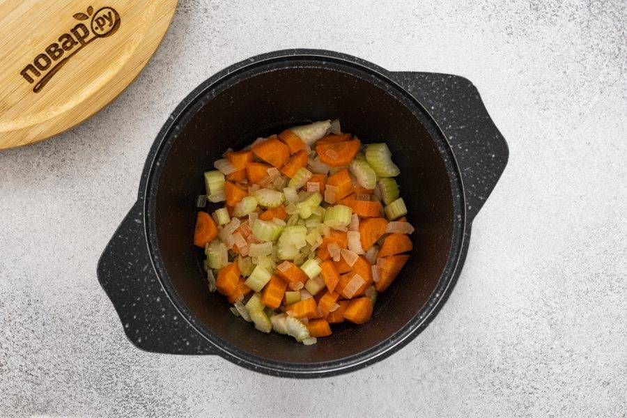 Морковь очистите и нарежьте ломтиками. Стебель сельдерея тоже нарежьте и добавьте овощи в кастрюлю. Обжаривайте пару минут.
