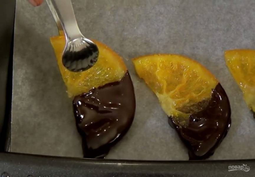 4. Выключите духовку, приоткройте дверцу и полностью остудите апельсины. Разрежьте пополам остывшие апельсины. Растопите шоколад на водяной бане, опустите каждую дольку в шоколад и выложите на бумагу для выпечки. 