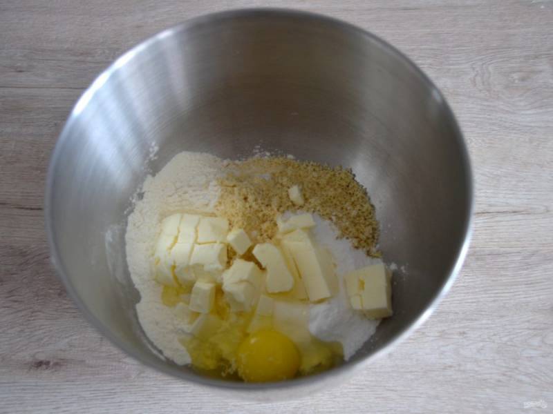 В емкость для замешивания теста всыпьте пшеничную и миндальную муку, соль, сахарную пудру, добавьте порезанное кубиком холодное сливочное масло, вбейте яйцо.
