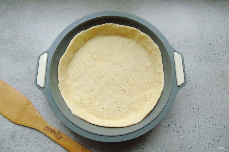 Тесто раскатайте и выложите в форму для выпечки, образуя бортики. Наколите тесто вилкой.