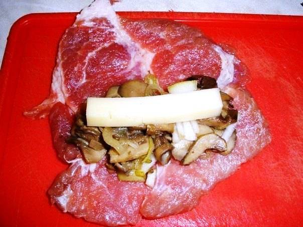 На кусочек мяса выложите часть грибов, пластинку сыра и сверните рулетом. Закрепите мясо зубочисткой или ниткой и сложите на противень.