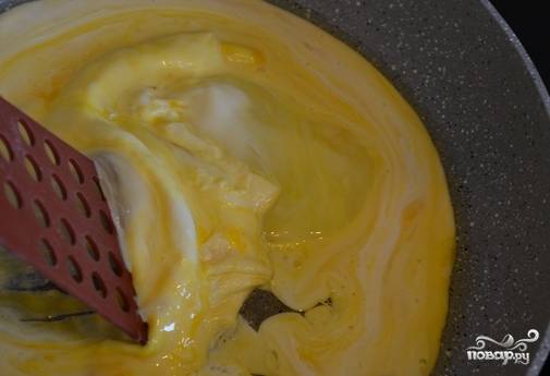 Выливаем яичную смесь на разогретую с маслом сковороду и буквально через несколько секунд, как только яйца схватятся, сдвигаем лопаткой схватившийся слой.