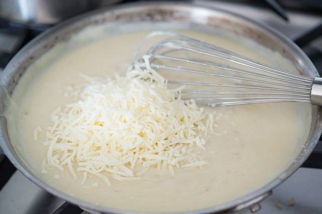 4. Влить на сковороду холодное молоко и как следует перемешать. Затем добавить тертый сыр и довести соус до однородной консистенции. При желании посолить и поперчить по вкусу. 
