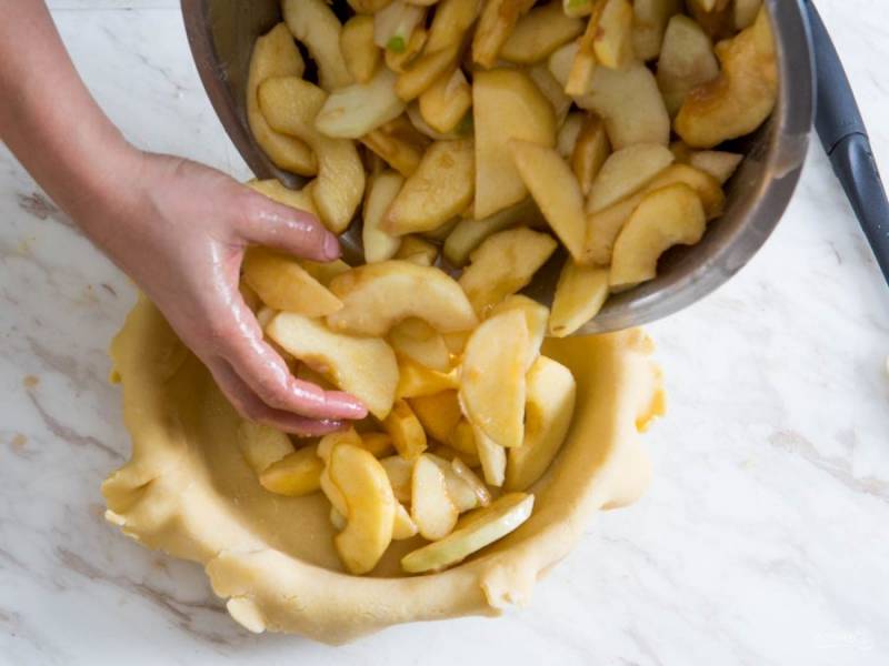 Форму для выпекания смазываем сливочным маслом, выкладываем раскатанный пласт теста. Сверху распределяем начинку из яблок. 