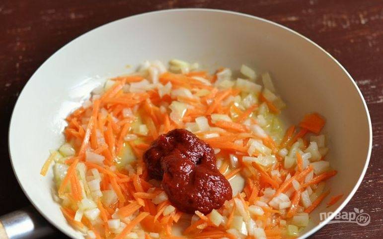 Очистите лук и морковь. Вымойте овощи, обсушите. Лук нарубите кубиками, а морковь натрите на терке. Пассеруйте овощи в сковороде с растительным маслом до золотистости, затем добавьте томатную пасту и перемешайте. 
