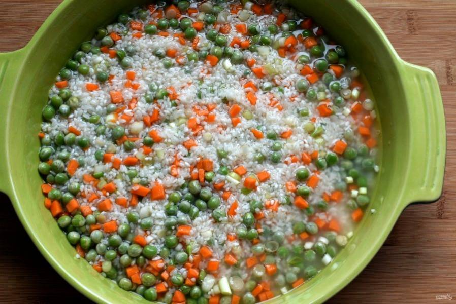Рис промойте и залейте кипятком на 10 минут, затем слейте. Морковь и лук  очистите и нашинкуйте мелкими кубиками. Смешайте рис с овощами, добавьте замороженный горошек, посолите и выложите все в глубокую форму для запекания. Влейте воды на палец выше риса.