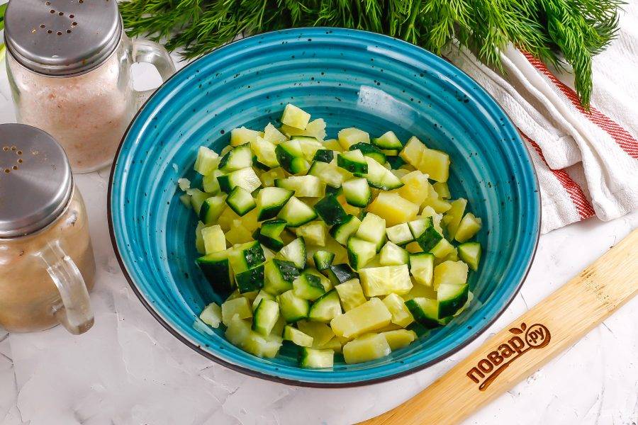 Промойте в воде огурец, срежьте хвостики с обеих сторон овоща, нарежьте такими же кубиками, как и картофель. Добавьте в емкость.