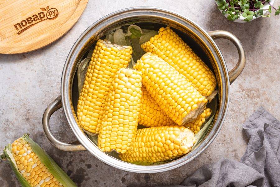 На дно кастрюли выложите пару листьев кукурузы. Добавьте кукурузные початки, влейте воду. Чтобы их было проще разместить, можно разломить початки пополам. Доведите до кипения и варите на умеренном огне до мягкости зерен. Чтобы кукуруза не всплывала, можно придавить ее тарелкой. По времени уйдет примерно 20-35 минут. Время приготовления будет зависеть от кукурузы, а готовность лучше определять на вкус. После опустите кукурузу в очень холодную воду, можно со льдом и оставьте так на минут 10. Так она станет мягче.