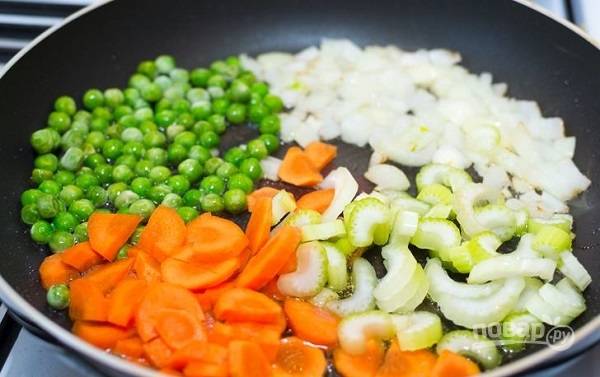 5. Готовую курицу остудите немного и нарежьте. На сковороде разогрейте растительное масло, добавьте к нему немного сливочного. Очистите и измельчите лук, морковь, стебель сельдерея. Выложите на сковороду, добавьте зеленый горошек. 
