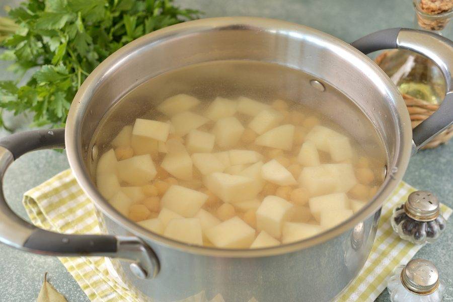 Переложите нут и нарезанный кубиком картофель в кастрюлю, залейте чистой водой, варите минут 5-7. 