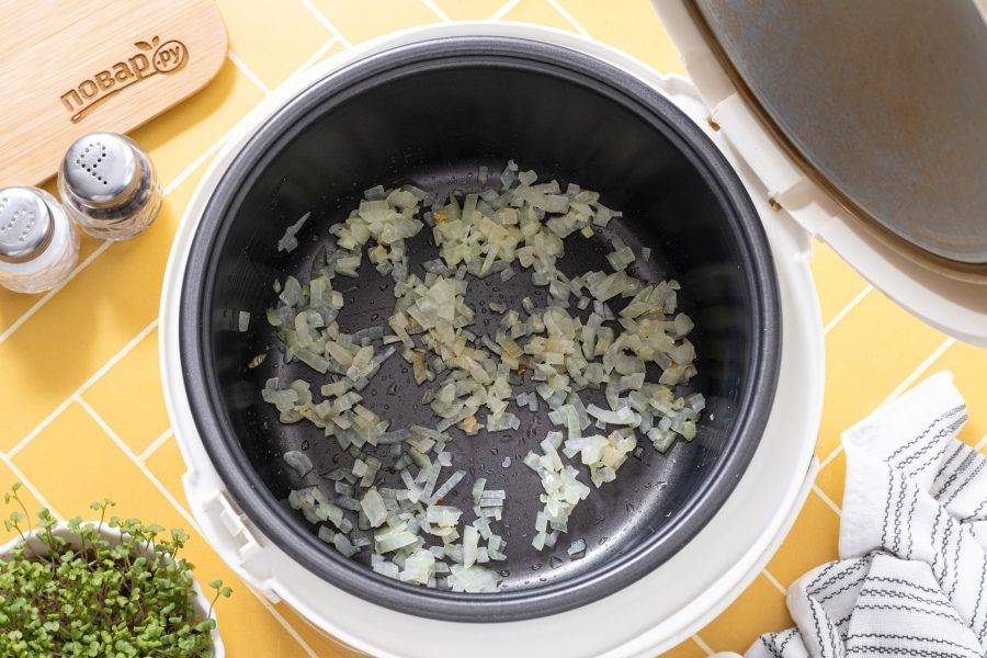 Влейте растительное масло в чашу мультиварки и разогрейте режиме «выпечка» или «подогрев». Затем обжарьте репчатый лук в режиме «выпечка» или «жарка» до мягкости и прозрачности.