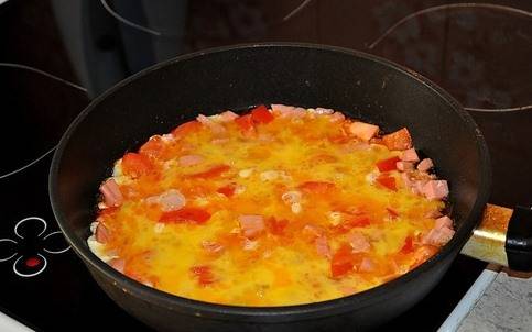 Немного обжариваем, перемешивая. Яйца слегка взбиваем венчиком или блендером и заливаем колбасу с помидорами.