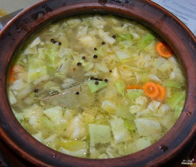 3. Подготовленные овощи (картошку и капусту нарежьте кубиками, морковь — кружочками) и обжаренное мясо выложите в глиняный горшочек, залейте горячим бульоном. Бульон предварительно заправьте немного обжаренной на сухой сковороде мукой.