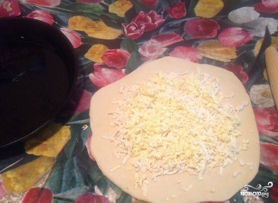 Присыпьте рабочую поверхность мукой, раскатайте тесто в тонкую лепешку. Натрите на терке твердый сыр, выложите его на раскатанное тесто. Сверху положите кусочек сливочного масла. 