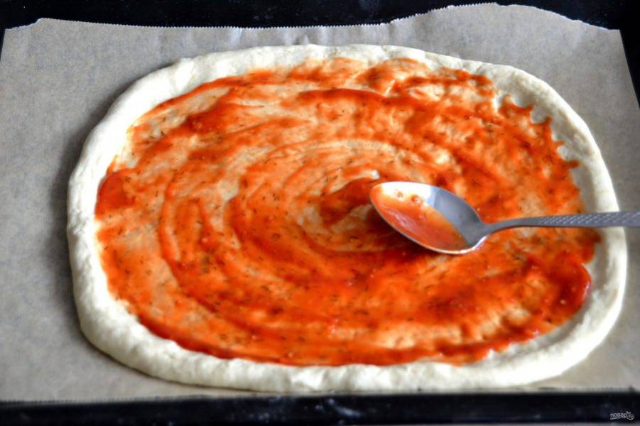 Нанесите на тесто томатный соус равномерным тонким слоем.