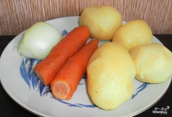 Прежде всего нужно отварить картофель и морковь. Это можно сделать в одной кастрюле. Просто обмойте овощи, залейте их водой и отварите до готовности, не очищая их. Когда они остынут, снимите с них кожицу и порежьте кусочками.