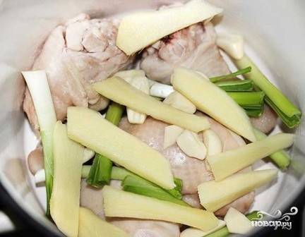 Выкладываем курицу в чистую кастрюлю, добавляем кусочки имбиря, белую часть от зеленого лука и зубчики чеснока. 