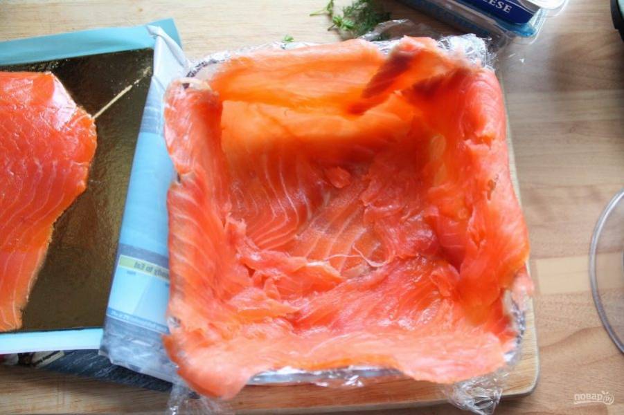 Прямоугольную форму застилаем пищевой пленкой и укладываем на дно и на бока формы тонкие пластинки лосося внахлест друг на друга.