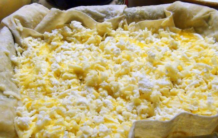Вливаем 2 ст.л. растопленного масла и обильно присыпаем сыром (творог+ сулугуни). Поливаем еще раз маслом и вливаем пол стакана кефира с яйцами.
